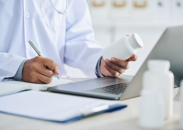 unrecognizable-female-doctor-with-laptop-holding-medication-writing-prescription